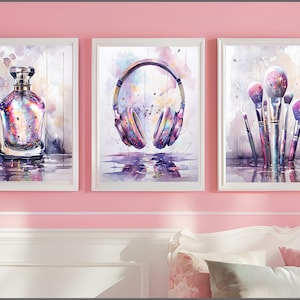Op de afbeelding: Een set van drie ingelijste aquarelprints. De prints tonen een parfumfles, een koptelefoon en make-up borstels. Het kleurenpalet omvat roze, paars en wit, met een reflecterend watereffect aan de onderkant van elke print.