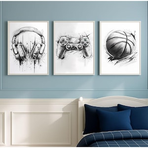 Puede incluir: Conjunto de tres láminas artísticas en blanco y negro enmarcadas. Las láminas representan unos auriculares, un mando de videojuegos y una pelota de baloncesto. La obra de arte tiene un estilo de boceto con efectos de salpicaduras de tinta.