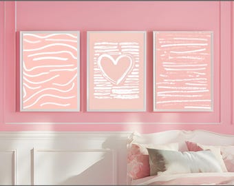 Op de afbeelding: Drie ingelijste kunstdrukken met abstracte ontwerpen in een roze kleurenpalet. De prints hebben witte penseelstreken en een hartvorm. De frames zijn wit en het kunstwerk wordt op een roze muur weergegeven.