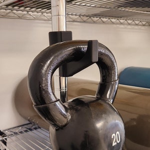 May include: A black kettlebell with a weight of 20 pounds hanging from a metal rack. The kettlebell is hanging above a blue exercise ball.