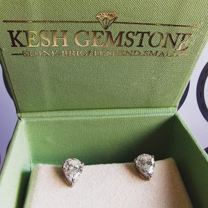 May include: A pair of pear-shaped diamond earrings in a green jewellery box with the text "KESH GEMSTONE - SHINE BRIGHT SPEND SMALL" on the lid.