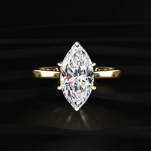May include: A gold engagement ring with a large, marquise-cut diamond. The diamond is clear and faceted, reflecting light. The ring has a simple, elegant band and four prongs holding the diamond.