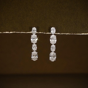May include: A pair of elegant drop earrings featuring a series of oval-cut, sparkling diamonds. The diamonds are arranged in a graduated design, with the largest at the bottom and the smallest at the top. The earrings are set against a dark brown background.