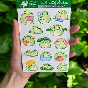 The frogs are shown doing everyday joyful activities: one frog holds a small book or notebook, another presents a tiny flower with a sweet smile, while another lounges peacefully with a relaxed expression. Several frogs are interacting with nature—one hides in grass, another holds autumn leaves, one wears a leafy “hat,” and another stands proudly holding a bright sunflower. There is also a frog soaking happily in a small blue tub, adding a cozy self-care vibe to the collection.