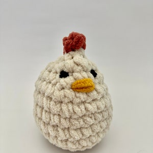 May include: A white crocheted chicken toy with a red comb, black eyes, and a yellow beak.