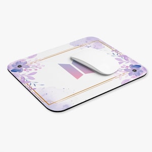 Könnte beinhalten: Ein weißes Mauspad mit einem lila und rosa Aquarelldesign. Das Design zeigt ein stilisiertes Logo mit einem floralen Rand. Das Mauspad befindet sich auf einem weißen Hintergrund.