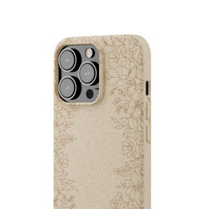 Pode incluir: Capa de telefone bege com um padrão floral. A capa tem uma superfície texturizada e apresenta um padrão detalhado de flores e folhas em uma cor bege mais escura. As lentes da câmera são visíveis no canto superior esquerdo.