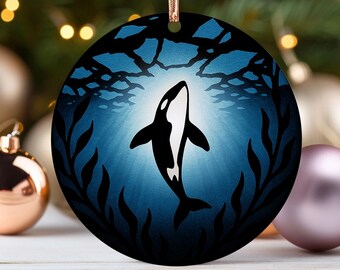 May include: Round Christmas ornament featuring a black and white orca whale swimming upwards in a blue underwater scene. The ornament has a gold string for hanging and is surrounded by decorative elements.