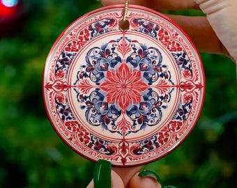 May include: A round ceramic ornament with a red, white, and blue floral design. The ornament has a gold string for hanging.