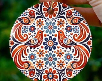 May include: A round ceramic ornament with a colorful folk art design. The ornament features two birds, flowers, and swirling patterns in red, orange, blue, and white. It has a gold string for hanging.