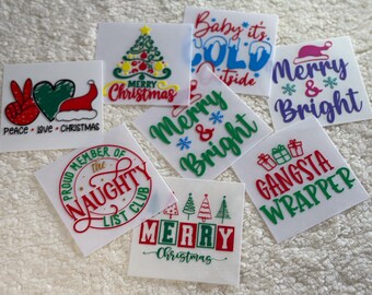 May include: A collection of nine Christmas-themed iron-on transfers featuring various designs and phrases, including "Merry Christmas", "Peace Love Christmas", "Baby it's Cold Outside", "Merry & Bright", "Proud Member of the Naughty List Club", "Gangsta Wrapper", and "Merry Christmas" with a row of Christmas trees.