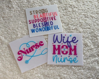 May include: Three white square stickers with colorful text. The first sticker says "Strong, Beautiful, Supportive, Blessed, Wonderful". The second sticker says "Nurse" with a blue stethoscope. The third sticker says "Wife, Mom, Nurse".