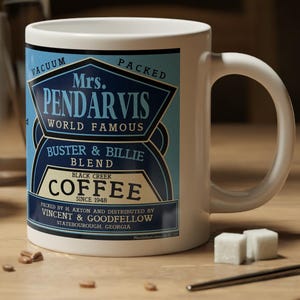 May include: White coffee mug with the text "Mrs. Pendarvis World Famous Coffee" in a blue and gold design. The mug is on a wooden surface with coffee beans, sugar cubes, and a spoon.