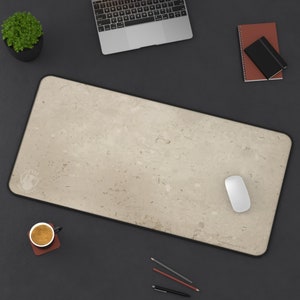 Könnte beinhalten: Eine beige Schreibtischunterlage mit schwarzem Rand und einem dezenten Muster. Eine weiße Computermaus liegt auf der Unterlage.