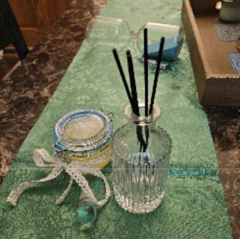 以下が含まれることがあります： 透明なガラス製のディフューザーボトルと、黒色のリード、透明なガラス製の蓋が青と白の蓋で覆われた、透明な液体が入ったガラス製の瓶。ディフューザーボトルは表面がテクスチャ加工されており、瓶は白いレースのリボンで飾られています。