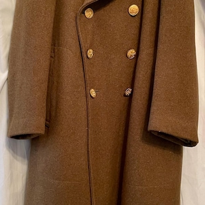 May include: A brown wool double-breasted overcoat with gold buttons and a blue patch on the right sleeve that says "HELLCAT".