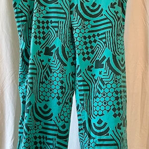 May include: Teal pants with a black and white geometric pattern. The pattern includes circles, squares, and lines.