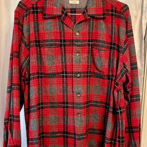 May include: A red, black, and gray plaid button-down shirt. The long-sleeved shirt has a classic collar, two chest pockets, and a button-up front. The shirt has a label that reads "McGregor".
