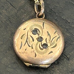 May include: A vintage gold-tone locket necklace. The round locket features an etched floral design with three dark accents. The necklace has a delicate chain.
