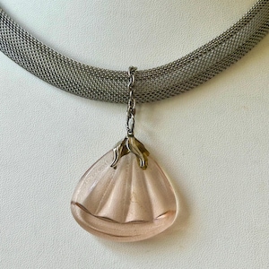 Peut inclure: Un collier en maille argentée avec un pendentif en forme de goutte d'eau rose clair. Le pendentif présente des lignes verticales et un dessus doré. Le collier est présenté sur un fond blanc.