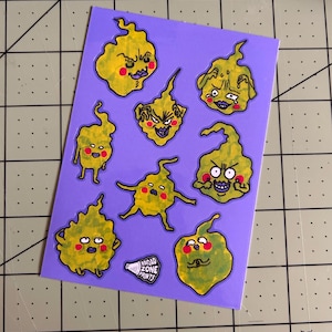 May include: A sheet of stickers with cartoonish, yellow, blob-like characters with various facial expressions. The stickers are on a purple background. The text "BROAD ZONE PRINTS" is visible on the sheet.