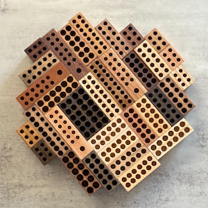 May include: A collection of rectangular wooden blocks arranged in a circular pattern. Each block features a grid of circular holes drilled into the surface. The wood varies in color from light tan to dark brown, showcasing natural grain patterns.