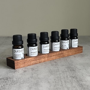 May include: A wooden essential oil rack with seven small glass bottles. The bottles are labeled with the names of different essential oils, including Eucalyptus, Bergamot, Ylang Ylang, Sweet Orange, Tea Tree, and Frankincense. The bottles are all in a dark brown color with white labels.