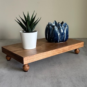May include: A wooden tray with four turned legs, featuring a small potted succulent plant and a blue ceramic planter shaped like a flower.