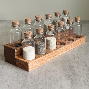 May include: A wooden rack with 12 small glass bottles with cork tops. The bottles are filled with different types of sand.