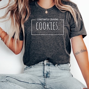 Könnte beinhalten: Ein dunkelgraues T-Shirt in Heather-Optik mit dem Aufdruck "CONSTANTLY CRAVING COOKIES." auf der Vorderseite.