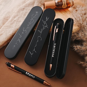 May include: Three black pen cases with gold accents. The cases are engraved with the names "Happy Camp", "Vanessa", and "Manu".