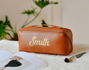 Peut inclure: Une trousse de maquillage de voyage en cuir marron avec une fermeture éclair dorée et le nom "Smith" brodé sur le devant.