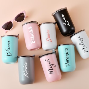 May include: An assortment of personalized tumblers in various colors, including pink, white, black, and teal, each with a name in elegant script. A pair of pink cat-eye sunglasses rests nearby. These insulated tumblers are ideal for beverages.