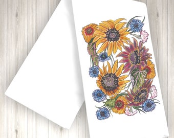 Op de afbeelding: Een witte keukendoek met een kleurrijk bloemenontwerp met zonnebloemen, paarse bloemen en blauwe bloemen.