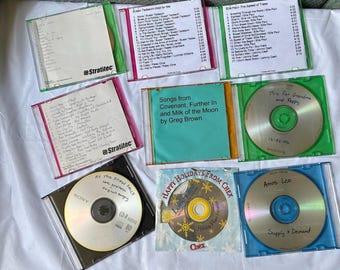 以下が含まれることがあります： 透明なプラスチックケースに入ったCDのコレクション。手書きのトラックリストが入っているものもあれば、印刷されたアルバムアートワークが表示されているものもあります。1枚のCDには、雪の結晶のデザインで「Happy Holidays from Chex」と書かれています。