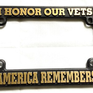 May include: Black plastic license plate frame with gold lettering that reads "I Honor Our Vets" on the top and "America Remembers" on the bottom.