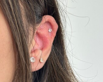 May include: Close-up of a person's ear with three small diamond earrings. The earrings are set in gold and are worn in the lobe, helix, and conch piercings.