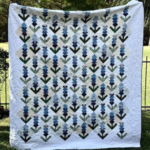 May include: A blue and green quilt with a pattern of bluebonnets. The quilt is made of various shades of blue, green, and white fabric.