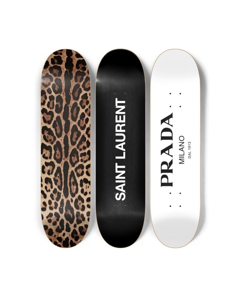 Puede incluir: Tres monopatines con dise&ntilde;os diferentes. Uno tiene un estampado de leopardo marr&oacute;n y negro, el segundo es negro con "SAINT LAURENT" en blanco, y el tercero es blanco con "PRADA MILANO DAL 1913" en negro.