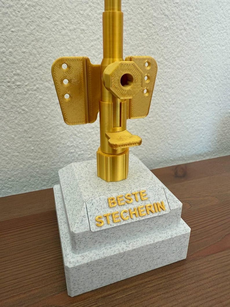 May include: A gold-colored trophy with a white base. The base has the words "BESTE STECHERIN" inscribed on it.