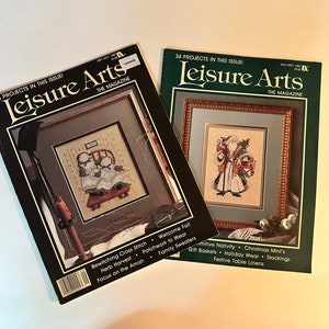 May include: Two copies of Leisure Arts magazine, a craft magazine. The September/October issue features a cross stitch pattern of a girl sitting on a stool. The November/December issue features a cross stitch pattern of Santa Claus holding a sack of gifts. Both issues feature the magazine's title in a black and white font on a green background.