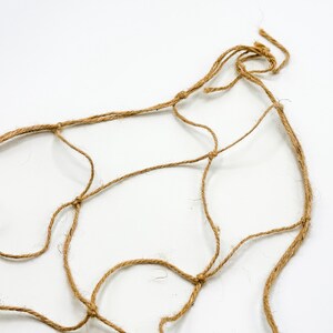 May include: A close-up of a brown, natural fiber rope net. The net is knotted and has a loose, organic shape.
