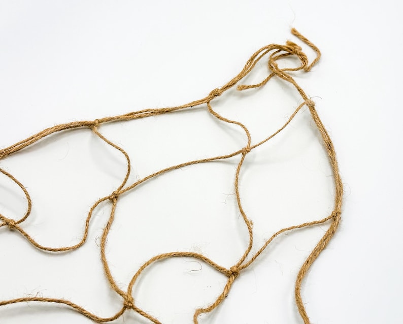May include: A close-up of a brown, natural fiber rope net. The net is knotted and has a loose, organic shape.