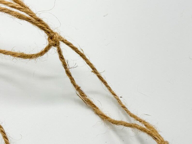 May include: Close-up of a brown, natural fiber rope tied in a knot.