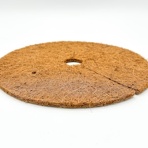 May include: A brown, round, coconut coir disc with a hole in the center. The disc is made of natural fibers and is used for gardening.