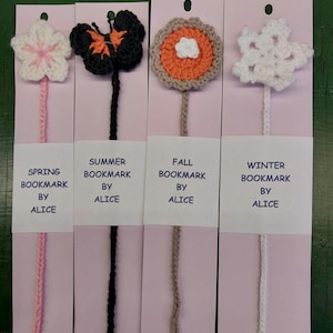 May include: Four handmade crochet bookmarks, each with a seasonal theme. The designs include a flower, butterfly, flower, and snowflake. Each bookmark has a different color stem and is attached to a pink card with the text "SPRING BOOKMARK BY ALICE", "SUMMER BOOKMARK BY ALICE", "FALL BOOKMARK BY ALICE", and "WINTER BOOKMARK BY ALICE".