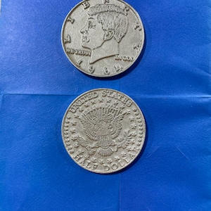 May include: Two silver Kennedy half dollar coins. The obverse of the top coin features a profile of John F. Kennedy and the date 1964. The reverse of the bottom coin shows the United States seal with an eagle.