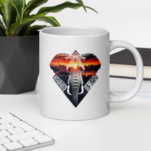 May include: White ceramic mug with a colorful graphic of an elephant's head with a sunset and city skyline in the background. The elephant's eyes are the sun setting over the city.