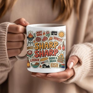 Puede incluir: Una taza de cerámica blanca con un collage colorido de ilustraciones y textos de temática sudafricana, incluyendo las palabras SHARP SHARP, HOWZIT, LEKKER, EISH y BRING & BRAAI, junto a iconos de una parrilla, carne, un sol y la bandera de Sudáfrica.