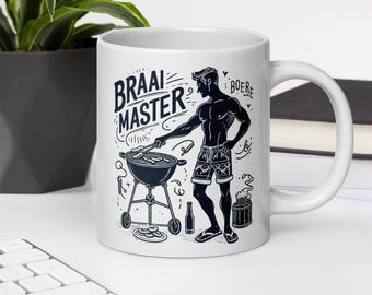 Op de afbeelding: Witte keramische mok met een zwart-witte illustratie van een persoon die barbecuet. De tekst "Braai Master" en "Boere" staat op de mok.